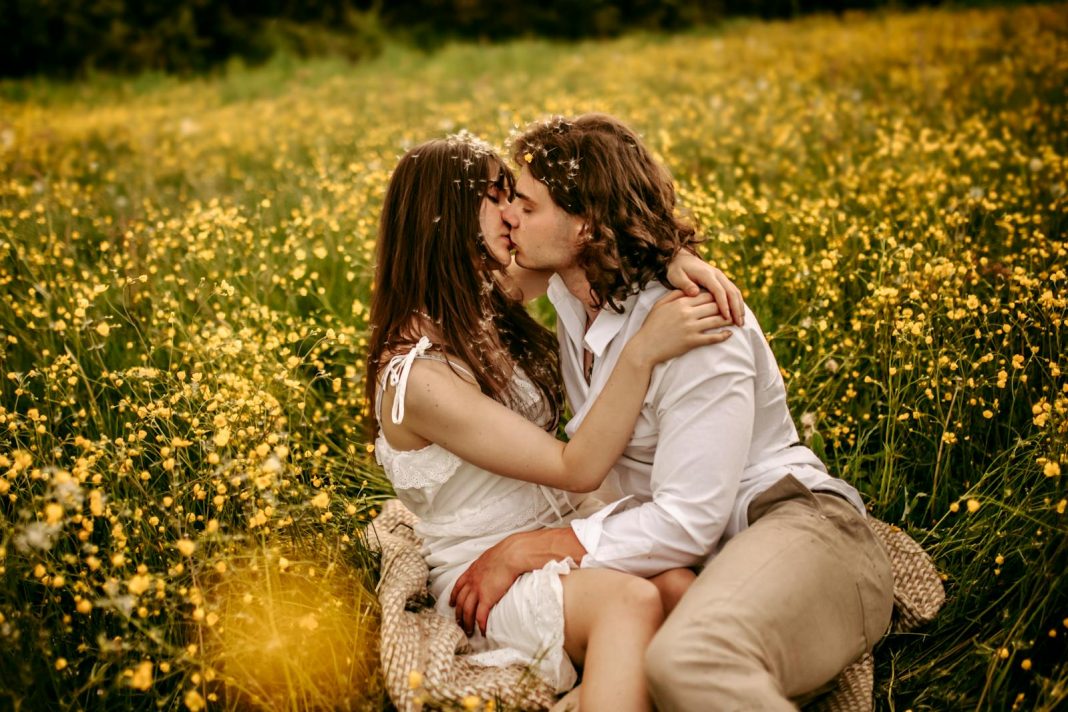 An embracing couple sharing a kiss amidst a blooming meadow, embodying love and romance.